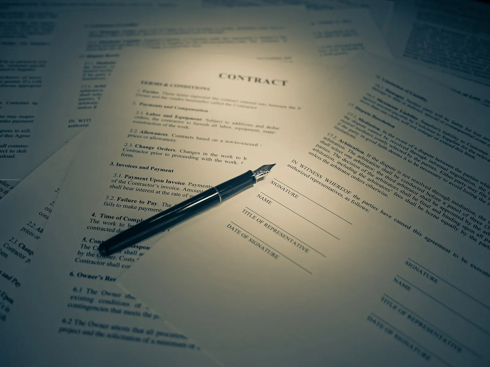 A typed contract under a desk lamp, with a pen resting on it