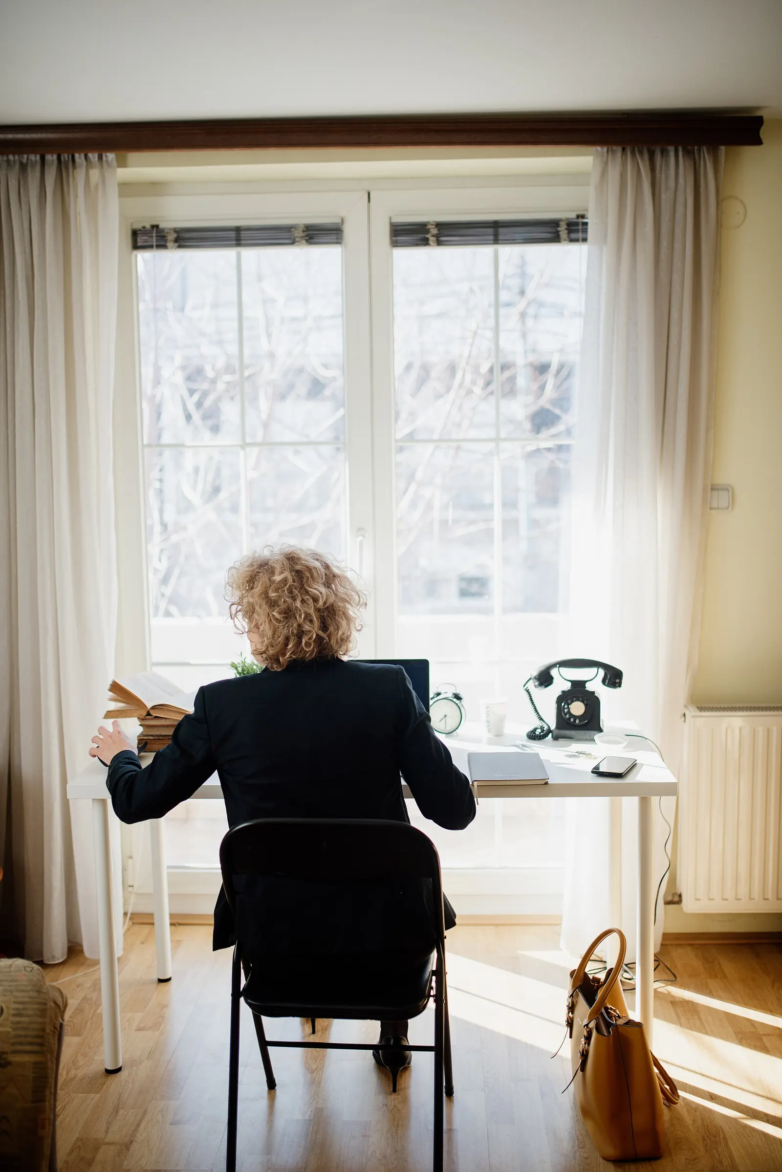 A woman at a desk by a bright window, next to a desk phone