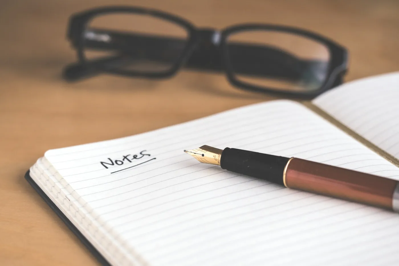 A fountain pen resting on an open notebook marked Notes