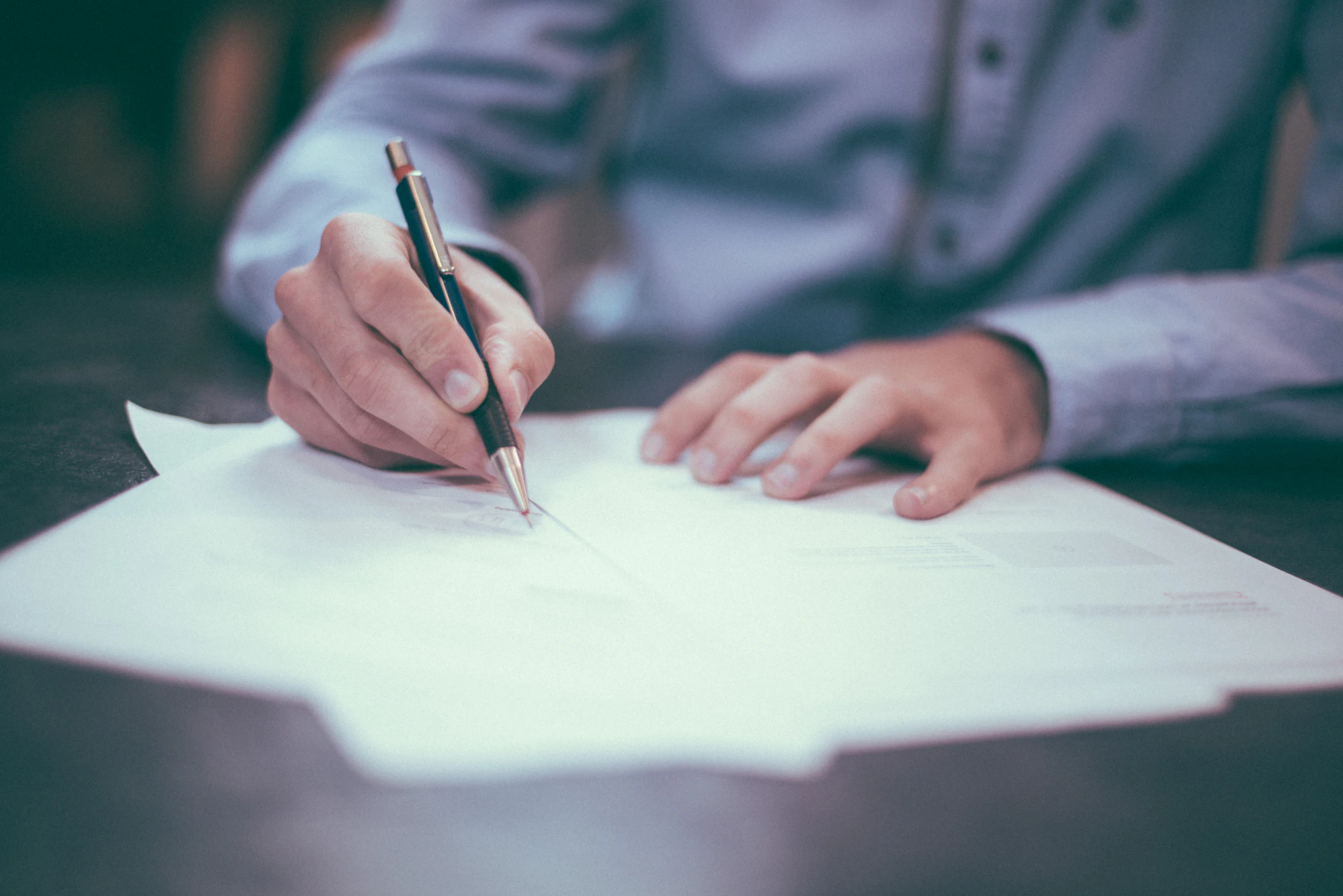 A hand signing a sheet of paper at a desk
